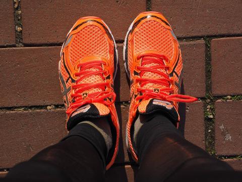 Neon orange running shoes. taken from above by person wearing them, they are wearing black running leggings and gray socks. red brick flooring. 