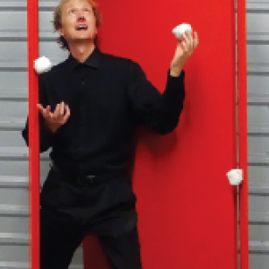 David Cousin standing in a red door way juggling 