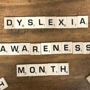 scrabble tiles spell out dyslexia awareness month on a wood background