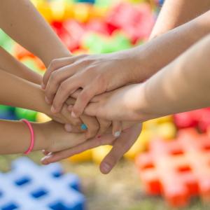 Children's hands holding hands like in a huddle, multicolored mats in background.